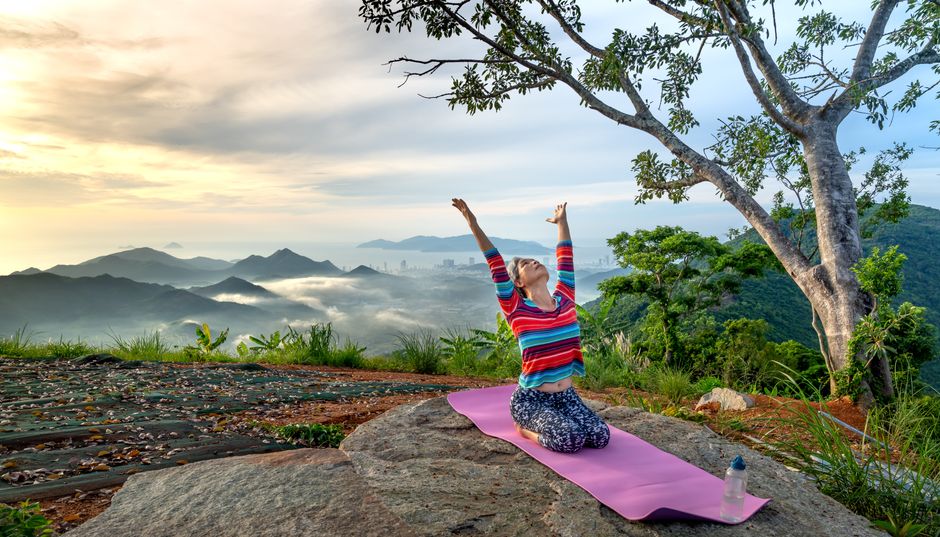 Woman practicing yoga at sunrise in nature on a hilltop with a beautiful mountain view.