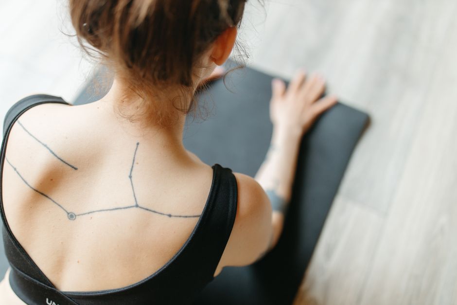 Back view of a woman practicing yoga with a constellation tattoo on her back.